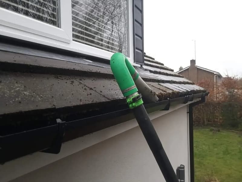 Green vacuum nozzle on a pole reaching black guttering below an upstairs window