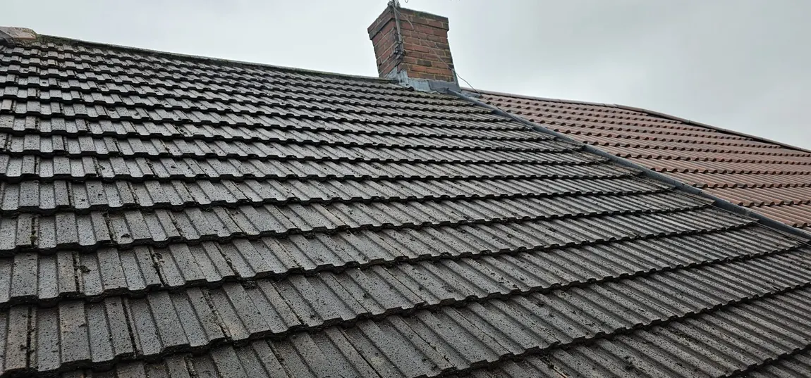 Grey tiled roof with little visible moss and a brick chimney